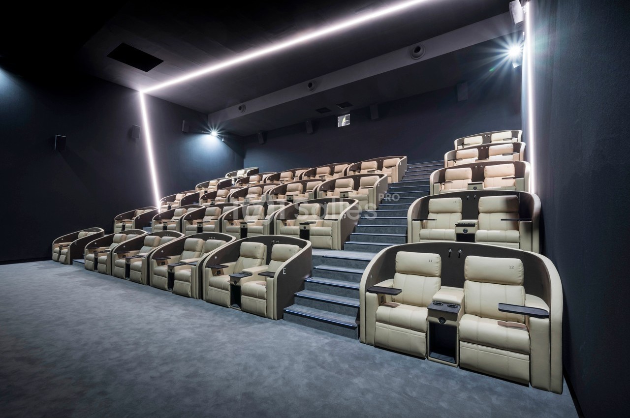 Salle de cinéma moderne avec sièges inclinables en cuir beige disposés en gradins et éclairage tamisé.