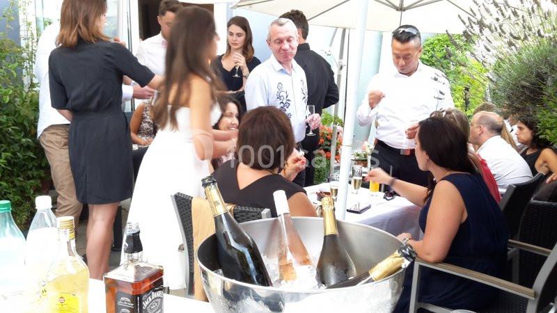Groupe de personnes discutant autour de tables en extérieur, avec un seau de bouteilles au premier plan.