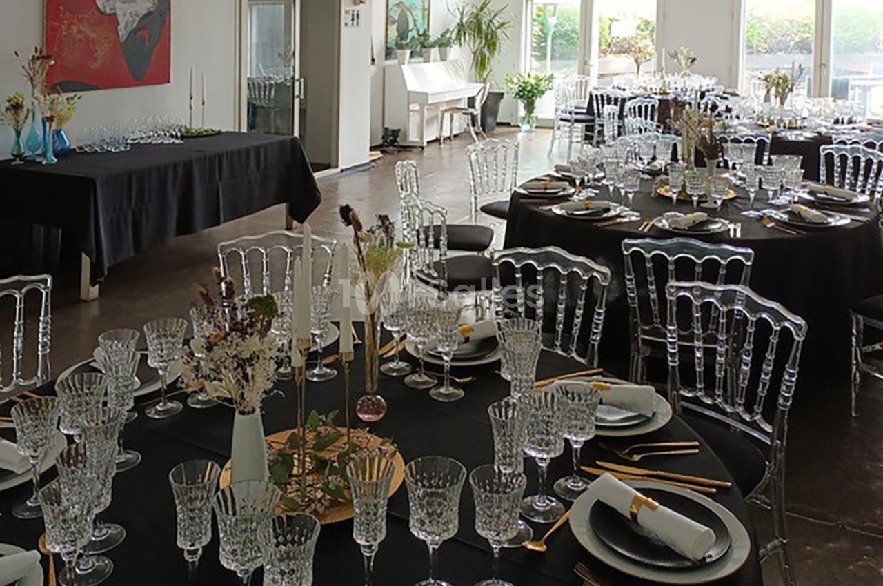 Salle de réception élégamment dressée avec des tables rondes noires, des chaises transparentes et une décoration florale.