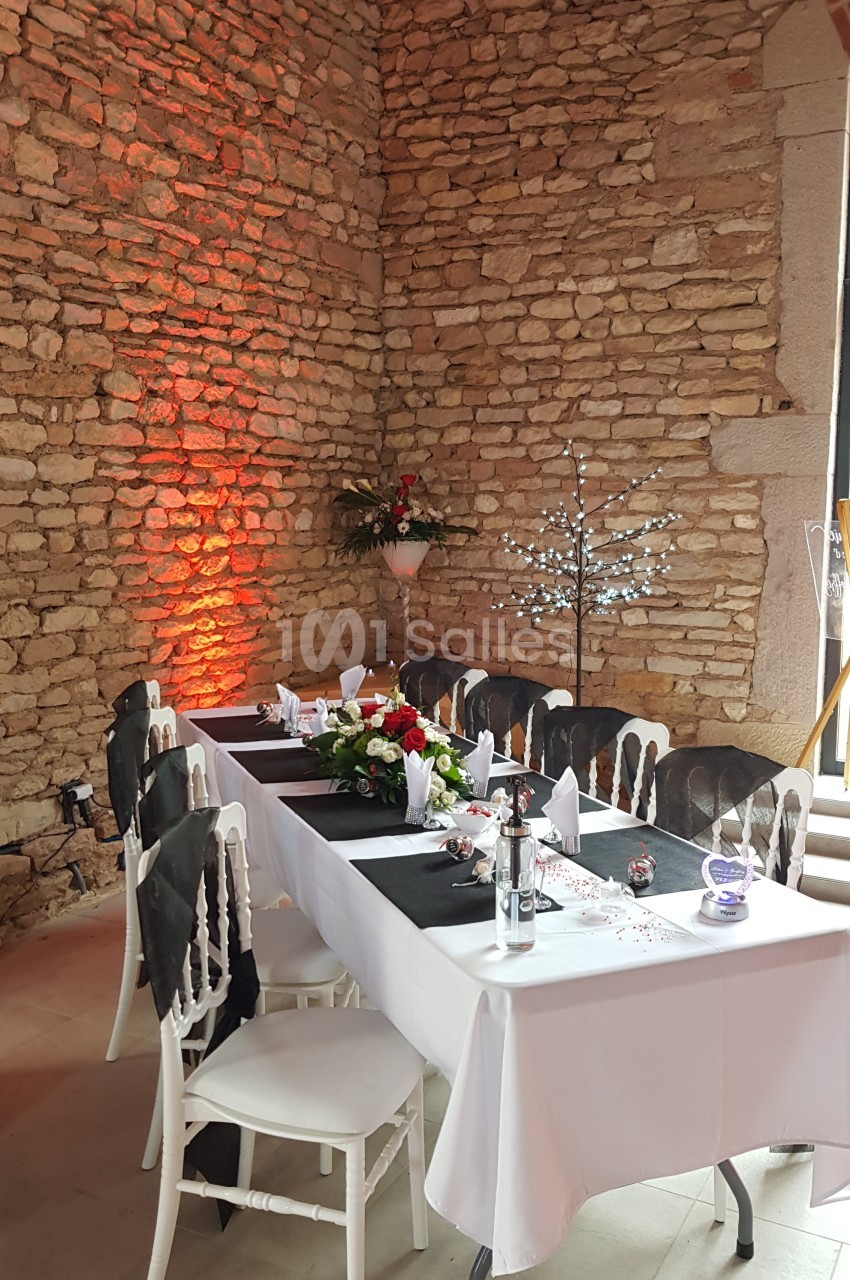 Table de réception décorée avec nappes noires et blanches, fleurs et bougies, dans une salle aux murs en pierre.