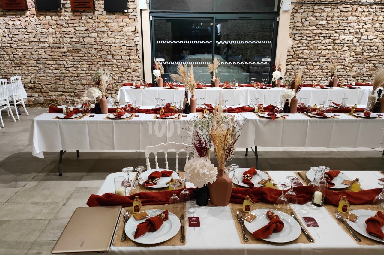 Tables de réception décorées avec nappes blanches, serviettes rouges, fleurs séchées et vaisselle élégante dans une salle en…