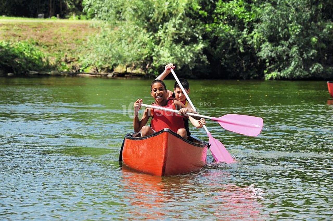 Deux personnes pagayant dans un canoë rouge sur une rivière entourée de végétation.