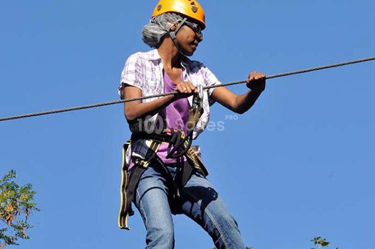 Une personne équipée d'un harnais et d'un casque traverse un parcours de tyrolienne sous un ciel dégagé.