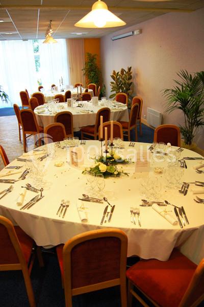 Salle de réception avec tables rondes dressées, nappes blanches, couverts, chandeliers et décorations florales.