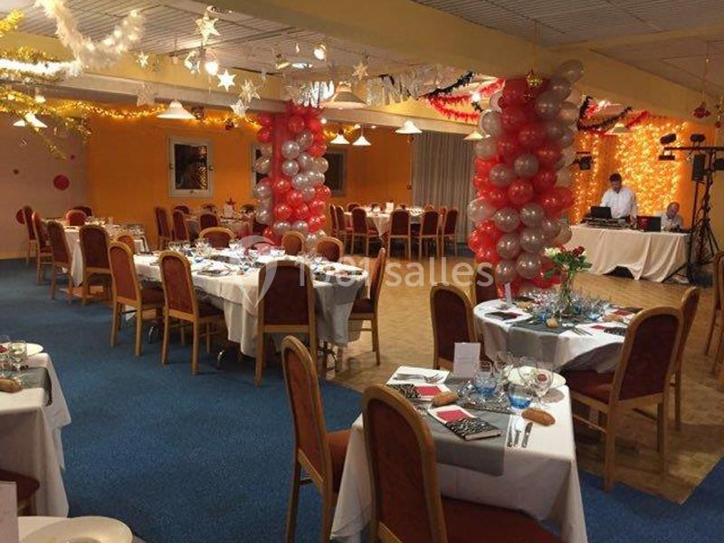 Salle décorée pour un événement festif, avec tables dressées, ballons colorés et éclairages chaleureux.