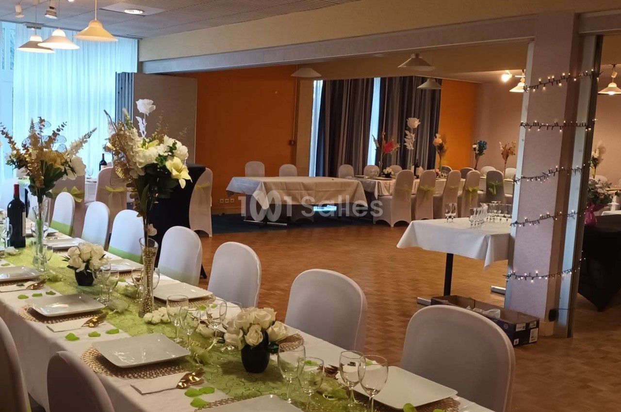 Salle de réception décorée avec des tables dressées, nappes blanches, centres de table fleuris et guirlandes lumineuses.