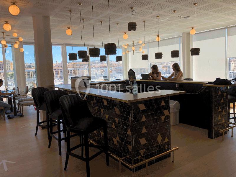 Espace lumineux avec un comptoir central en mosaïque, des chaises hautes et des suspensions modernes, vue sur un port.