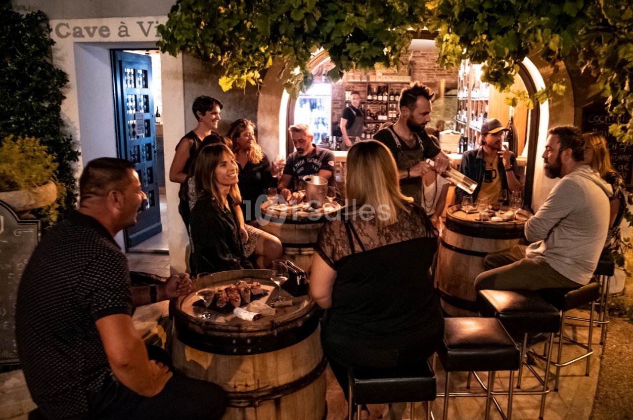 Groupe de personnes partageant un repas convivial autour de tonneaux dans une ambiance chaleureuse et éclairée.