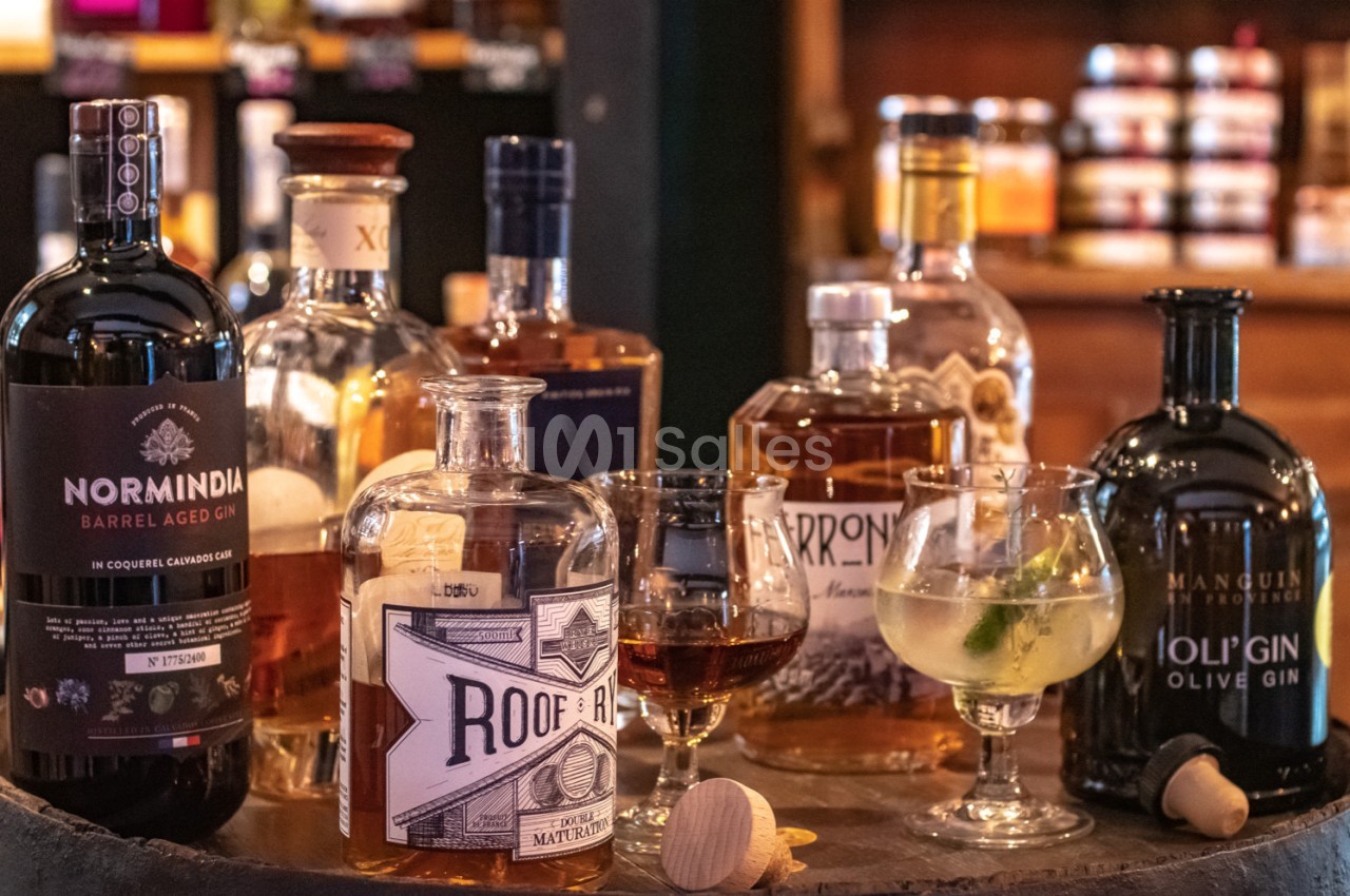 Bouteilles de spiritueux variés et verres servis sur un tonneau dans un cadre chaleureux de bar ou cave.