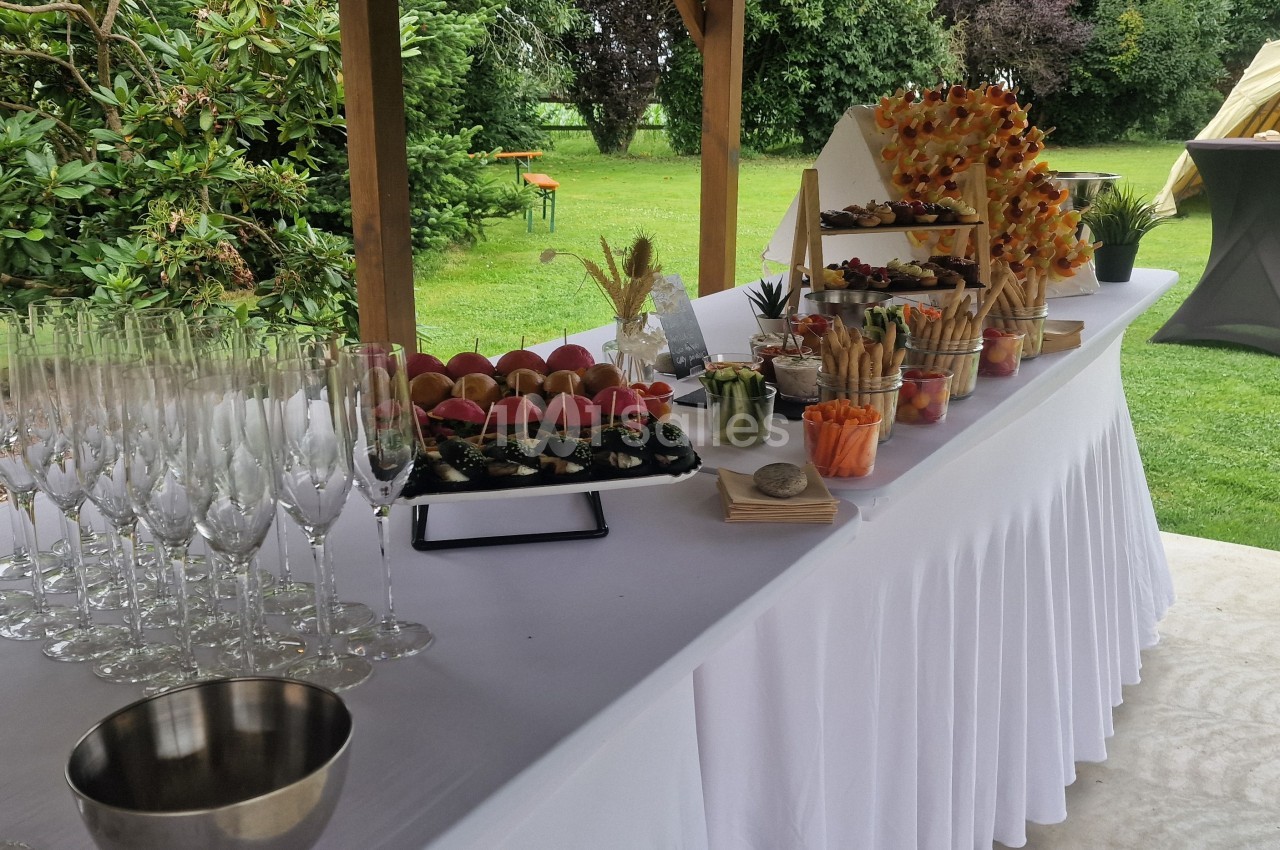 Table dressée en extérieur avec verrerie, amuse-bouches variés et décorations végétales sous un auvent.