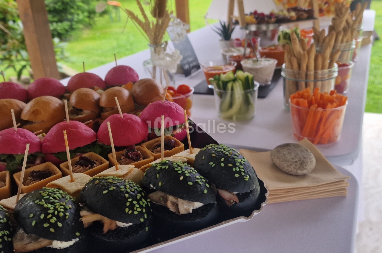 Plateau de mini-burgers colorés et verrines de légumes disposés sur une table pour un buffet en extérieur.