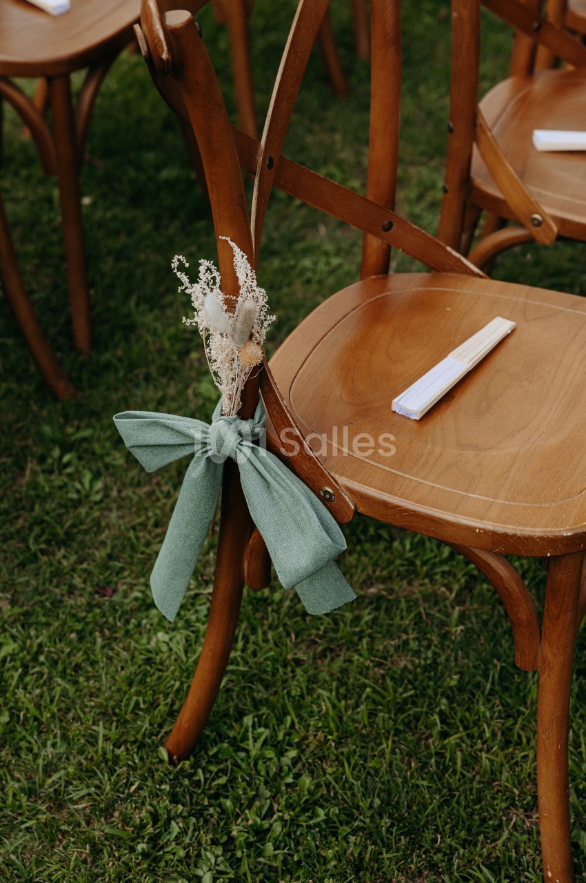 Chaise en bois décorée d'un ruban vert et d'un bouquet de fleurs séchées, placée sur une pelouse.