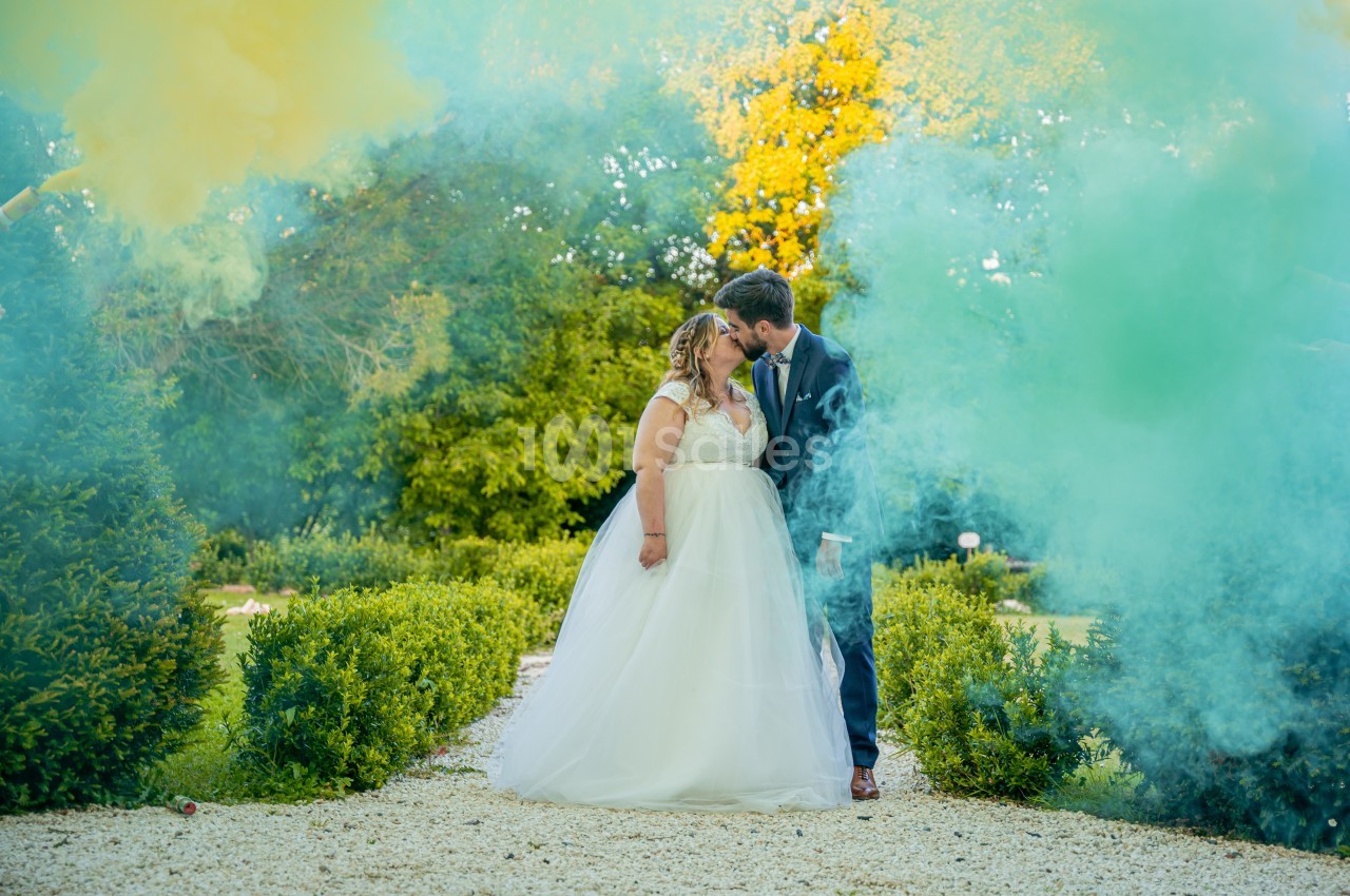 Un couple de mariés s'embrasse dans un jardin, entouré de fumée colorée jaune et verte.