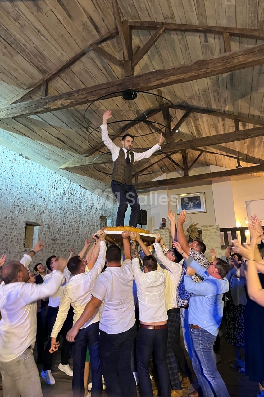 Un homme debout sur une chaise portée par une foule dans une salle avec un plafond en bois.