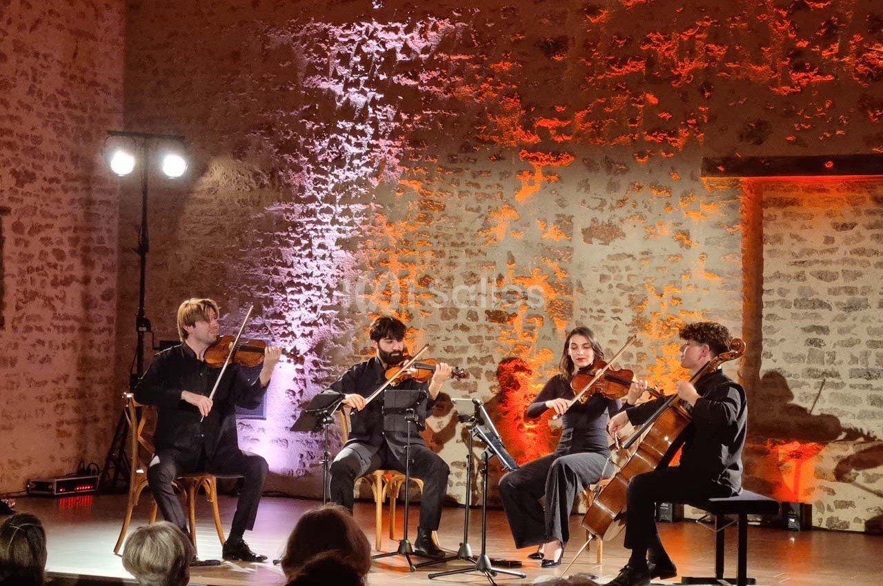 Quatuor à cordes jouant sur une scène éclairée, devant un mur en pierre avec des lumières colorées.