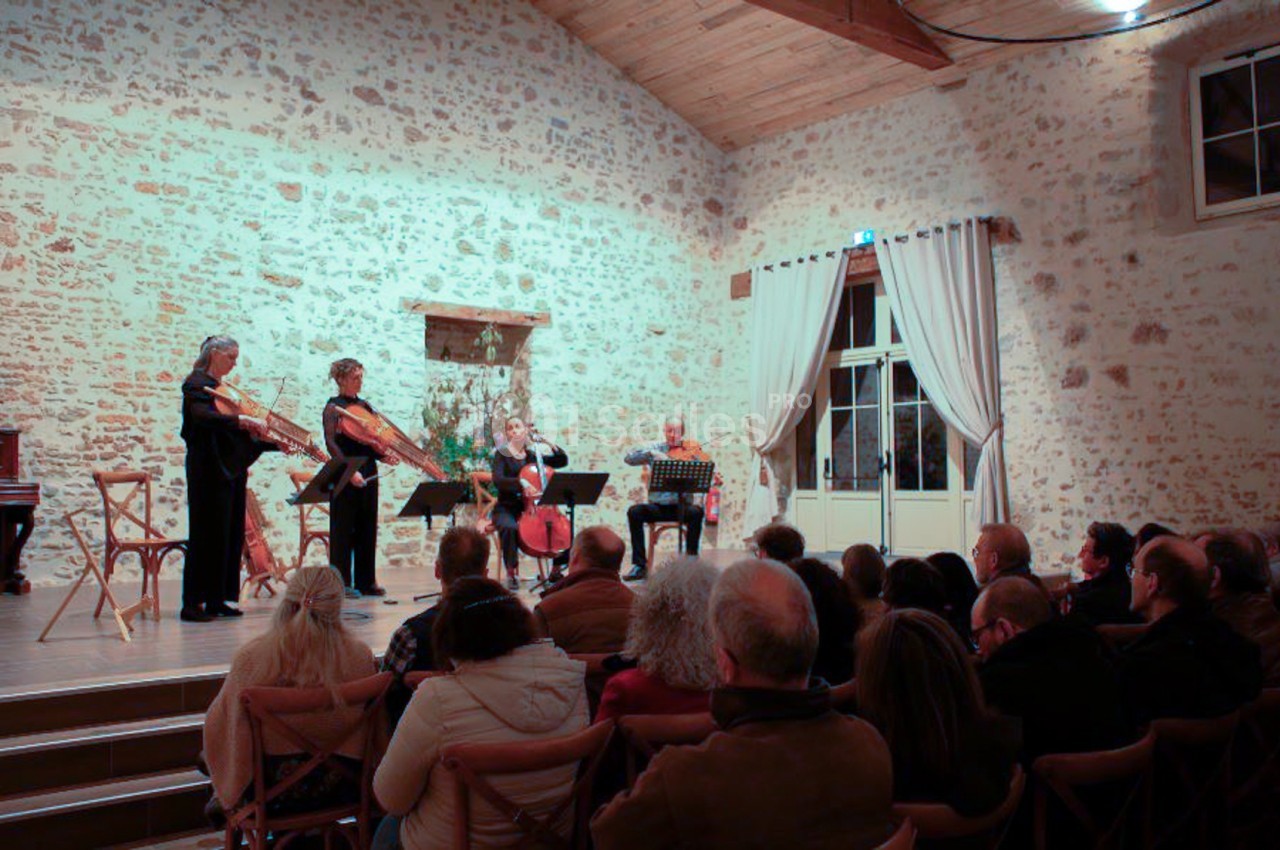 Un quatuor à cordes joue devant un public dans une salle en pierre avec un plafond en bois.