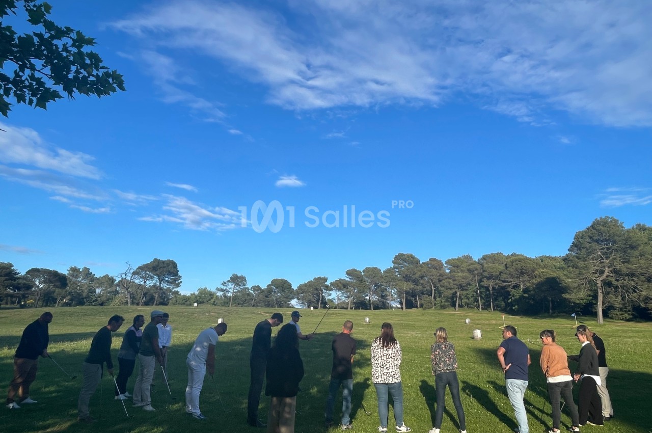 Un groupe de personnes se tient sur une pelouse sous un ciel bleu, observant ou participant à une activité en plein air.