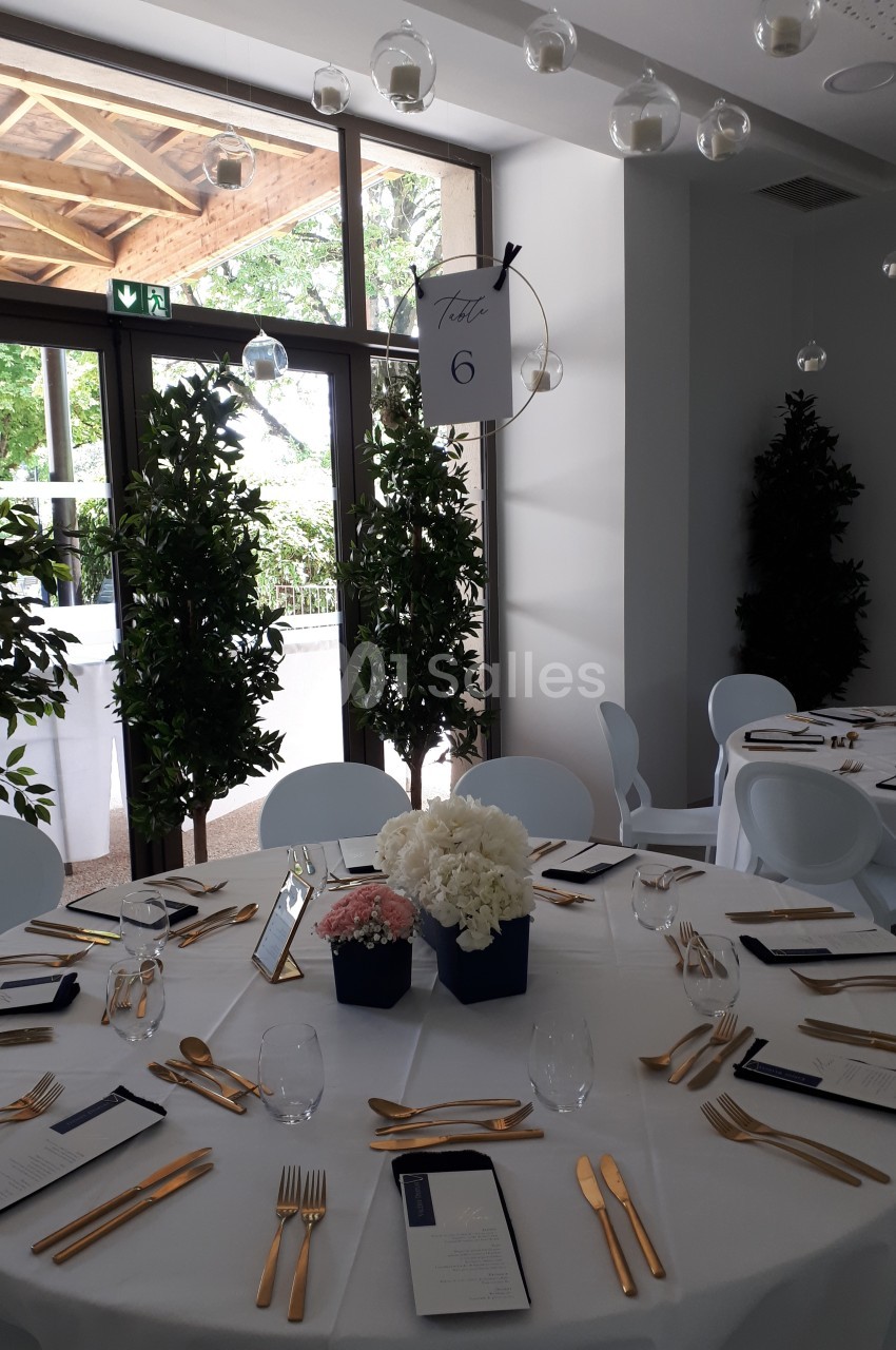 Salle de réception avec table ronde dressée, couverts dorés, centre de table floral et panneau indiquant ’Table 6’.