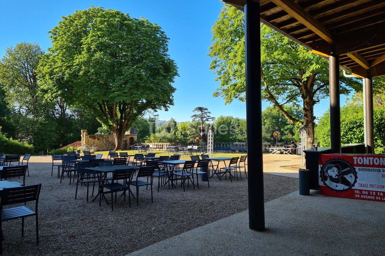 Terrasse extérieure avec tables et chaises, entourée d'arbres et d'un espace vert sous un ciel dégagé.