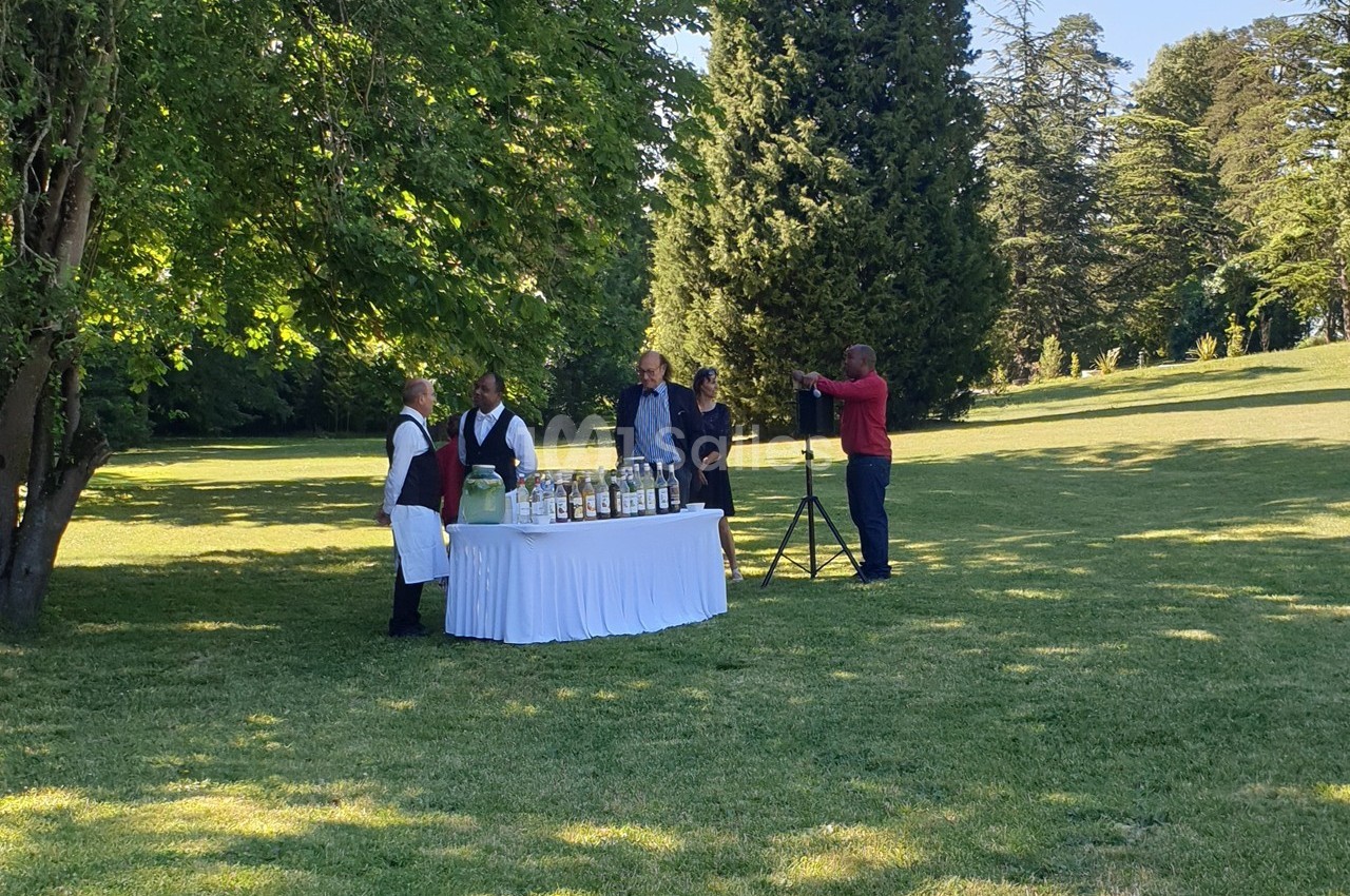 Un buffet en plein air avec un serveur et des personnes discutant dans un parc verdoyant.
