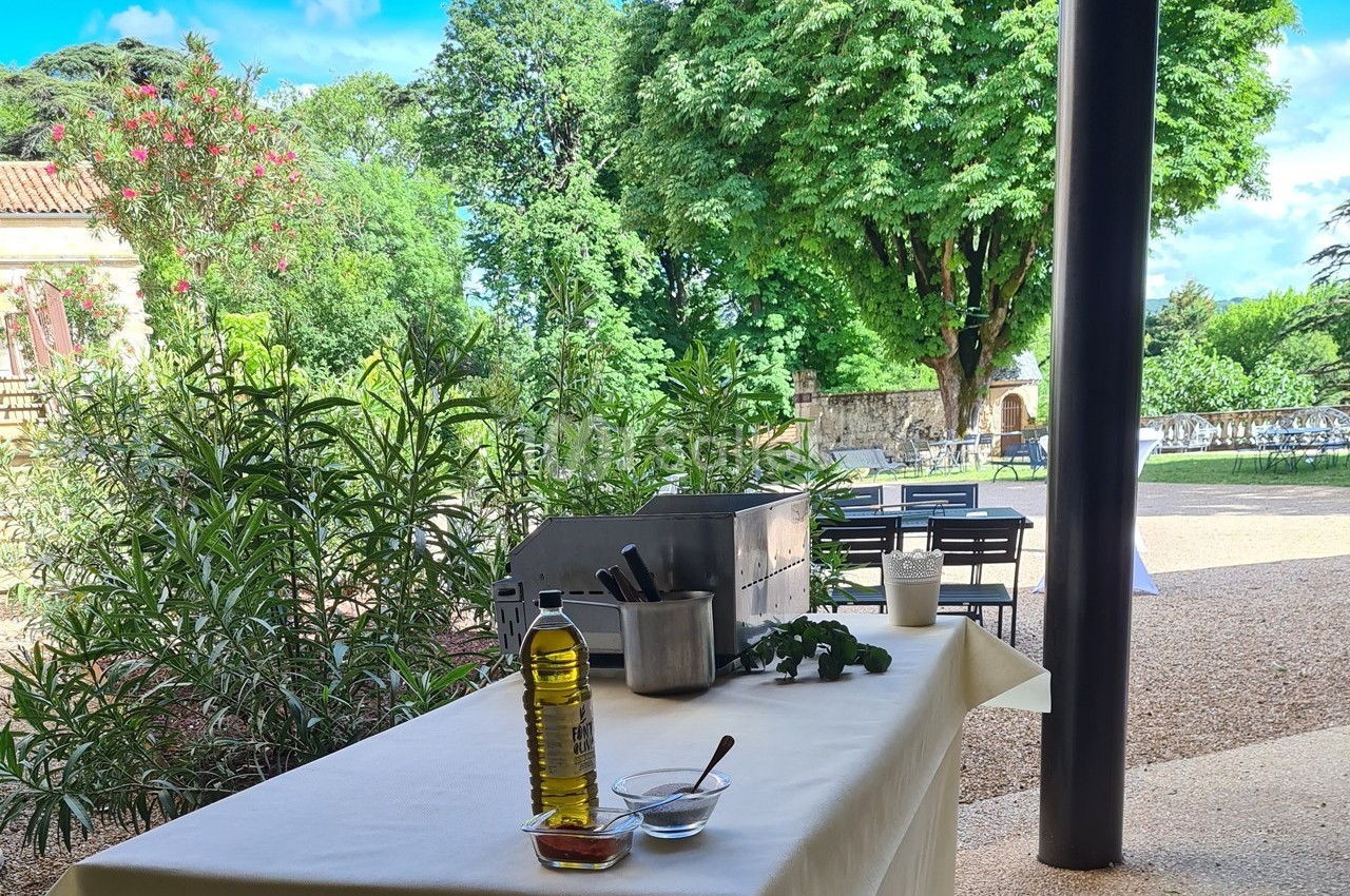 Table dressée en extérieur avec une bouteille d'huile d'olive, des herbes fraîches et des ustensiles de cuisine.