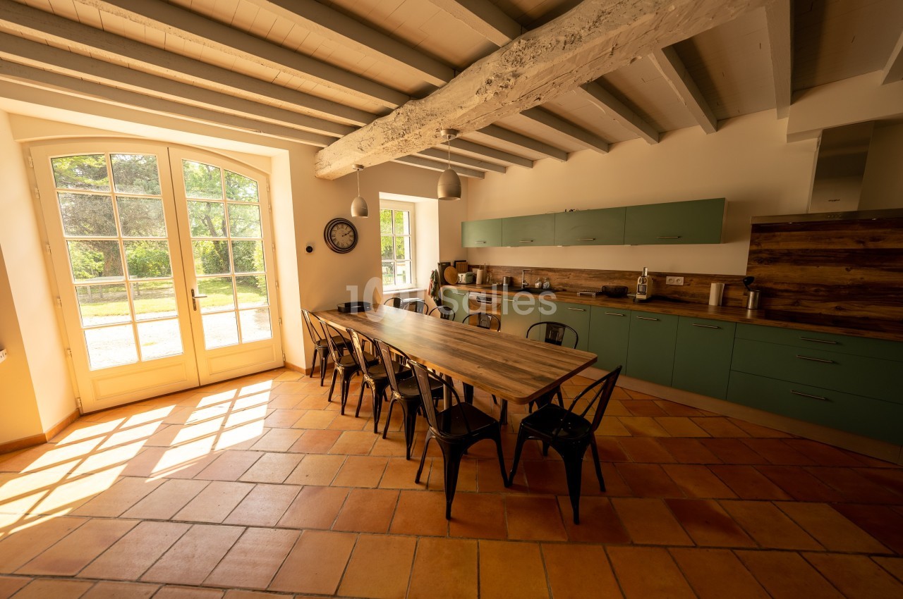 Cuisine lumineuse avec table en bois, chaises métalliques, poutres apparentes et vue sur un jardin par une grande baie…