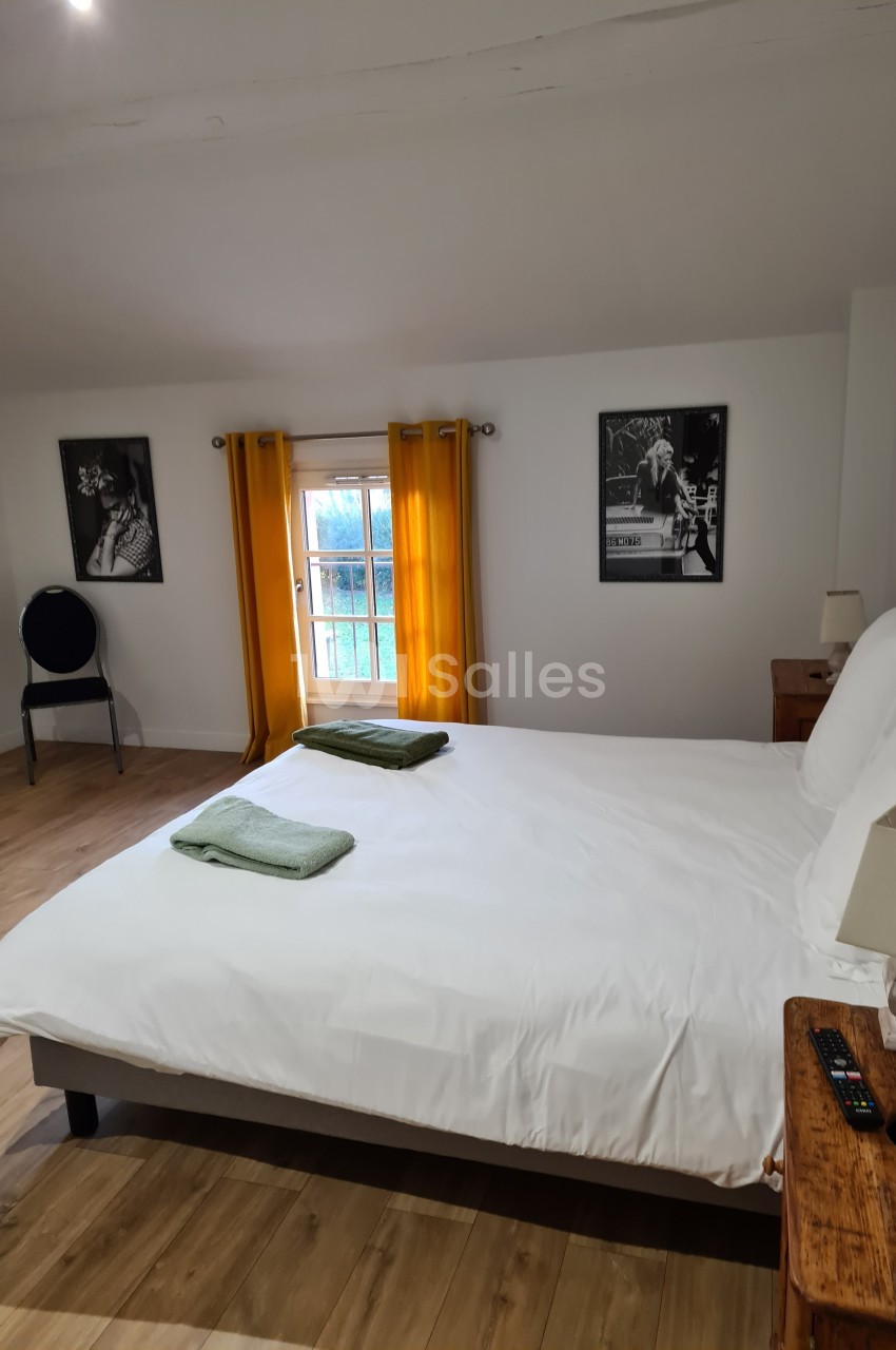 Chambre lumineuse avec lit double, draps blancs, serviettes vertes, rideaux jaunes et décorations murales en noir et blanc.