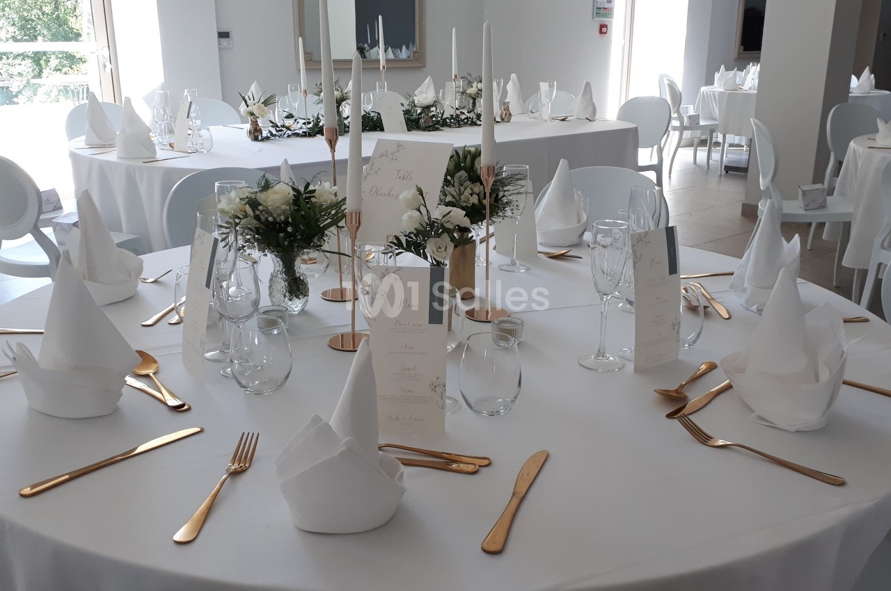 Table de réception élégamment dressée avec nappes blanches, couverts dorés, serviettes pliées et décorations florales.