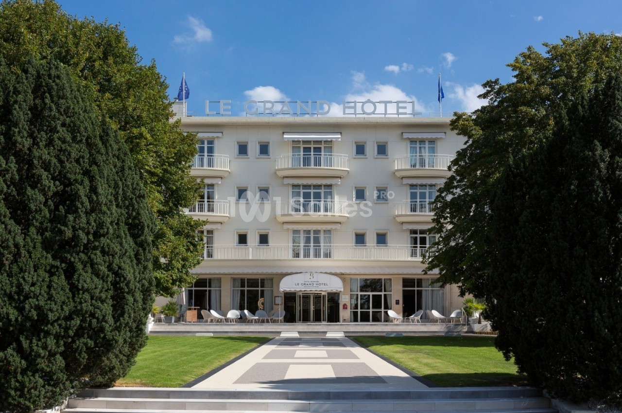 Façade d'un hôtel blanc entouré d'arbres, avec une allée centrale menant à l'entrée principale.