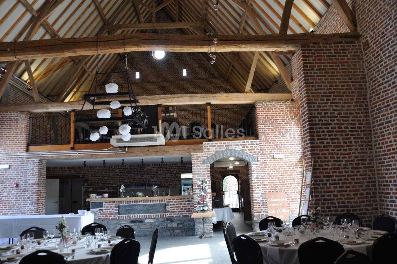 Salle de réception avec murs en briques, poutres apparentes et tables dressées pour un événement.