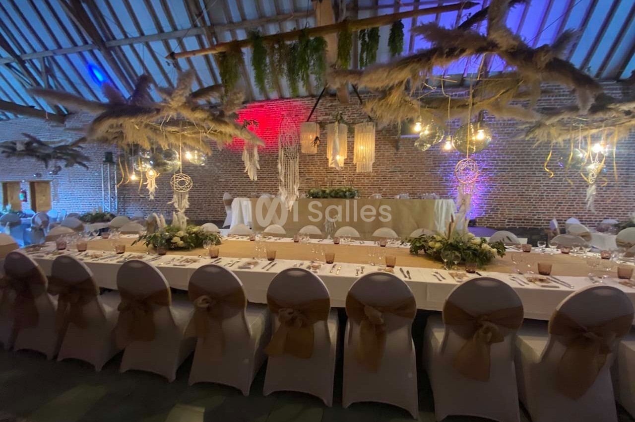 Salle de réception décorée avec des tables dressées, des chaises blanches et des suspensions végétales et lumineuses.