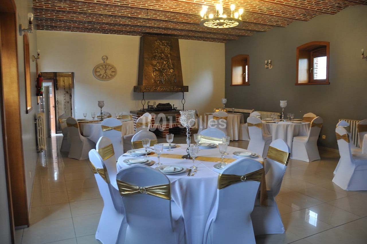 Salle de réception élégante avec tables rondes dressées, nappes blanches et chaises décorées de nœuds dorés.