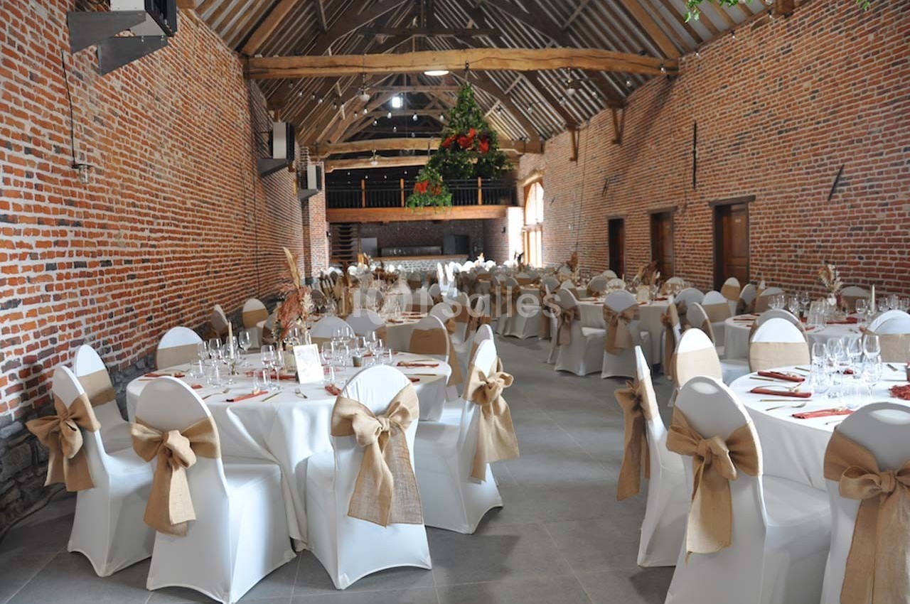 Salle de réception avec tables rondes dressées, nappes blanches et chaises décorées de nœuds en toile de jute.