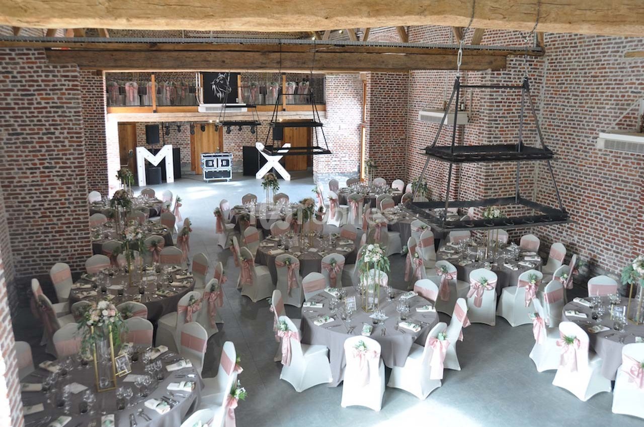 Salle de réception en briques avec tables rondes décorées de nappes blanches et chaises ornées de rubans roses.