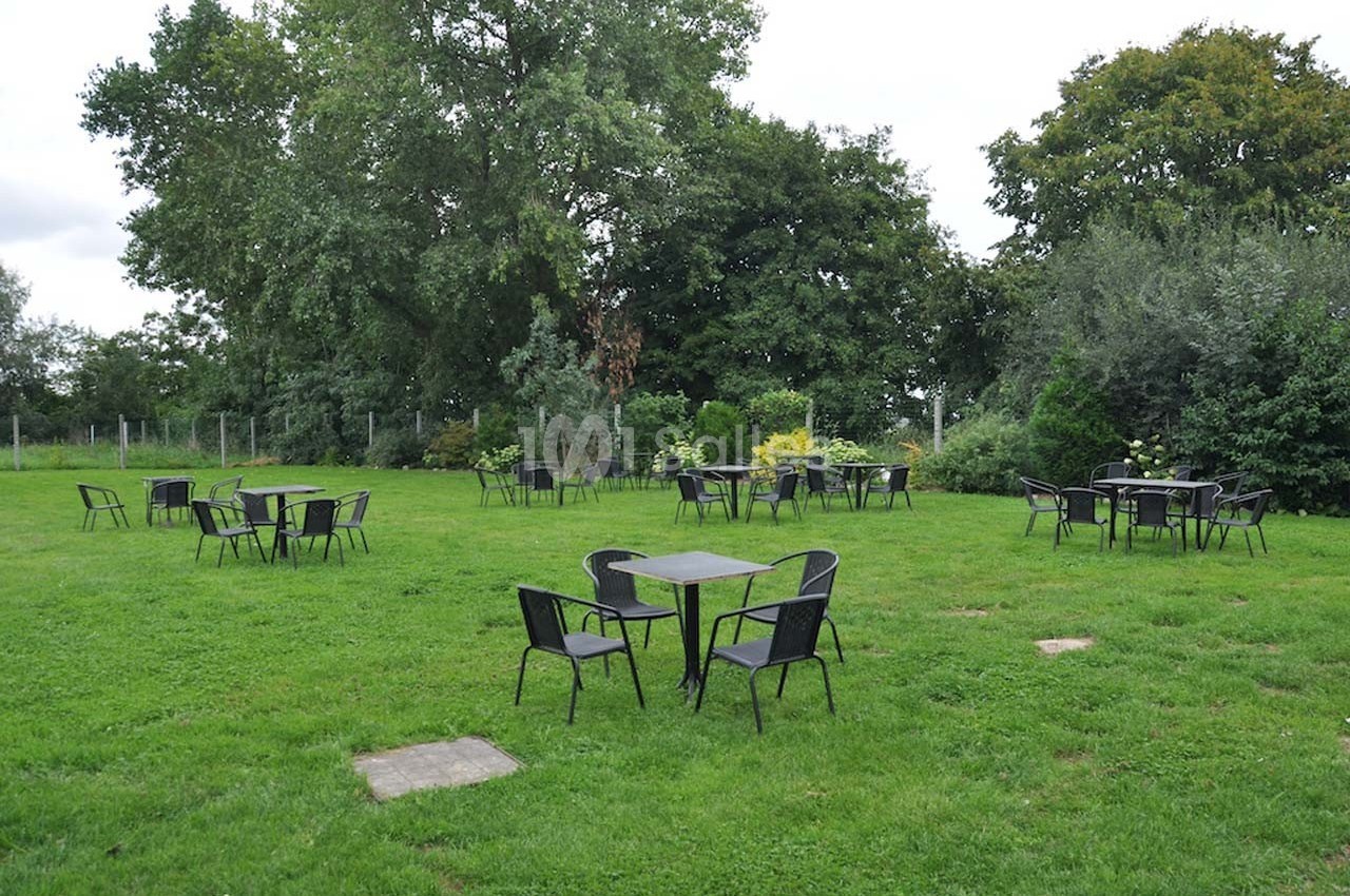 Tables et chaises noires disposées sur une pelouse verte entourée d'arbres et de buissons.