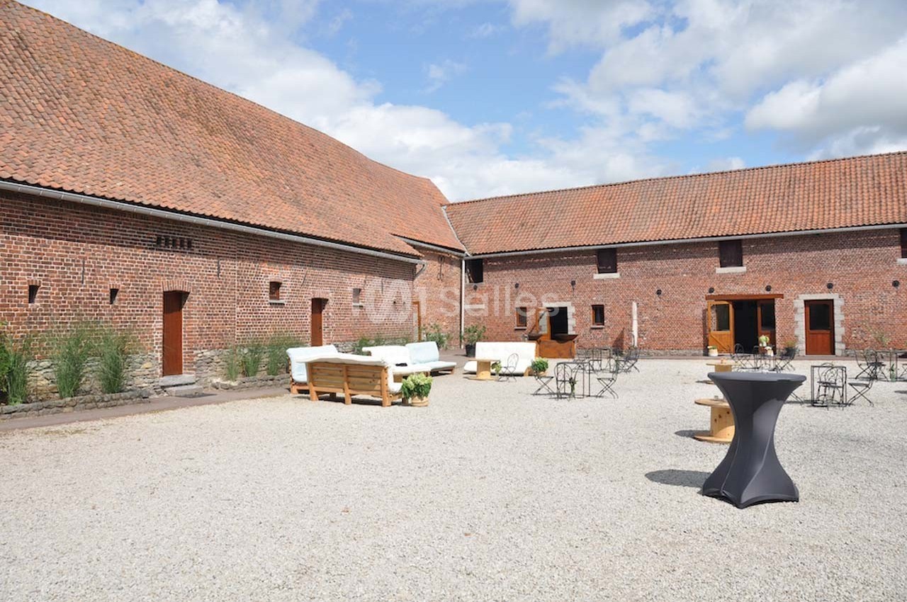 Cour intérieure d'une ferme rénovée avec murs en briques, mobilier de jardin et ciel partiellement nuageux.