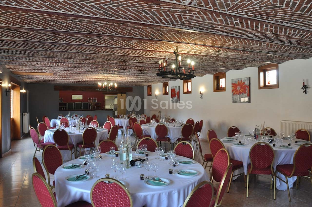 Salle de réception avec tables rondes dressées, chaises rouges et plafond en briques apparentes.