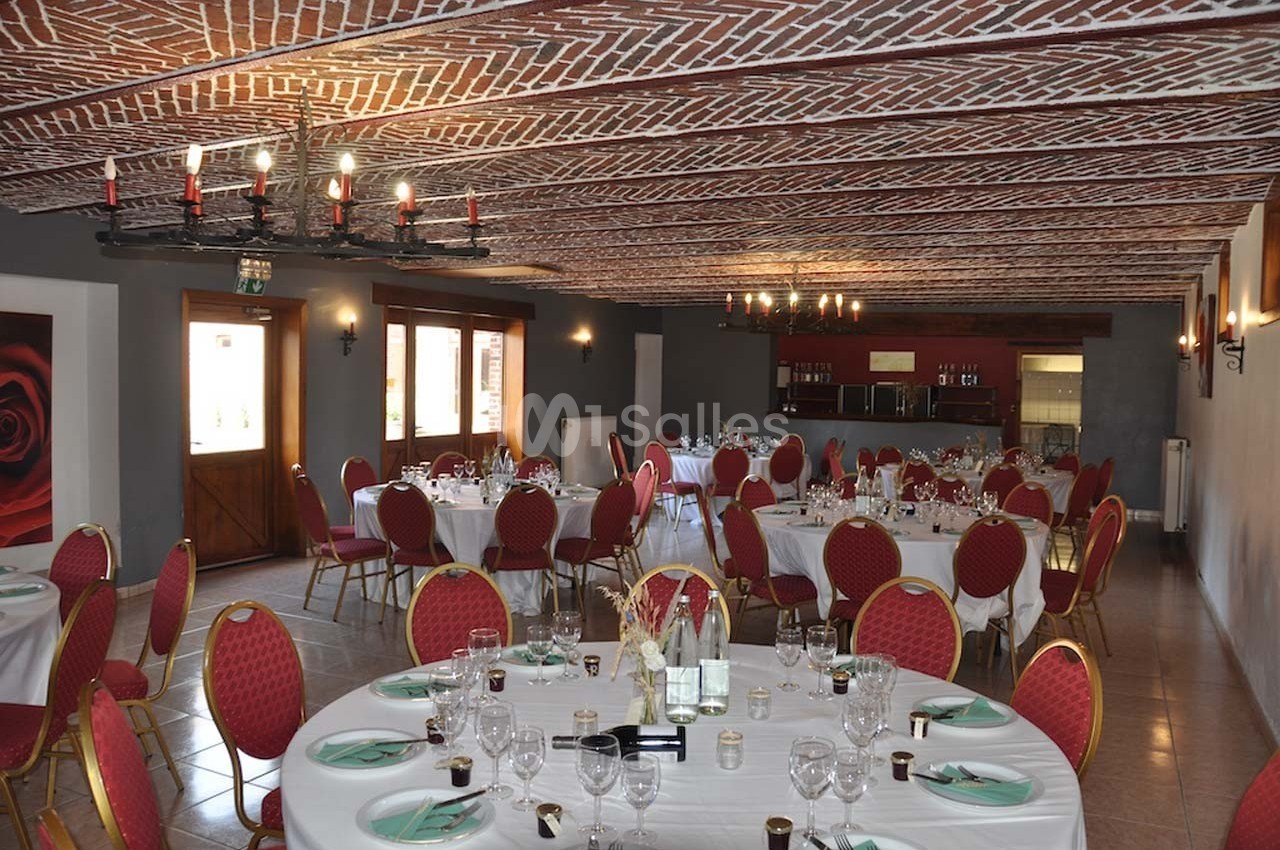 Salle de réception avec tables rondes dressées, chaises rouges et plafond en briques apparentes.