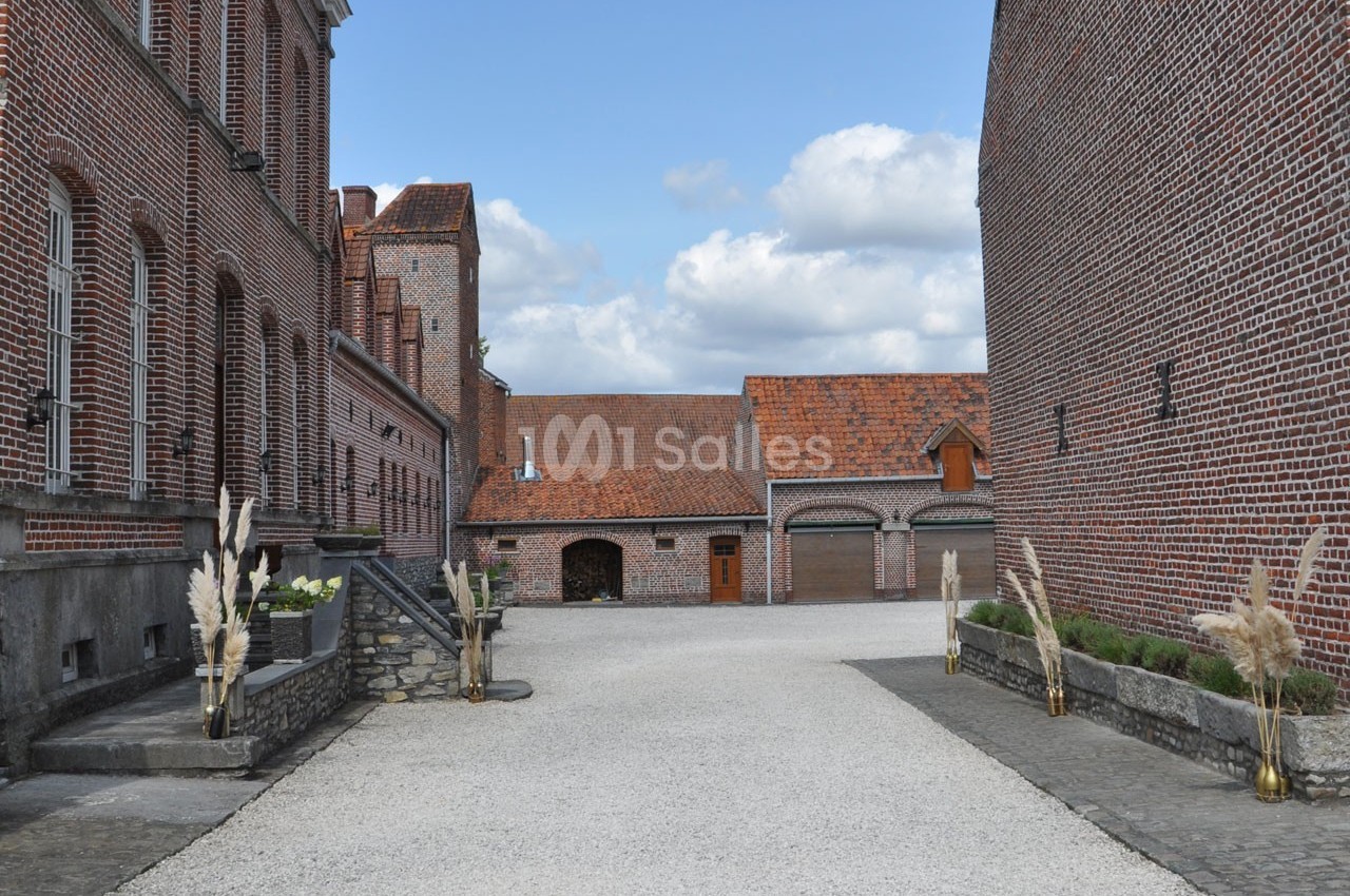 Cour pavée entourée de bâtiments en briques rouges avec des toits en tuiles et des décorations végétales.