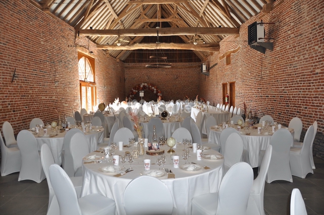 Salle de réception en briques avec tables rondes dressées, nappes blanches et décoration de mariage.