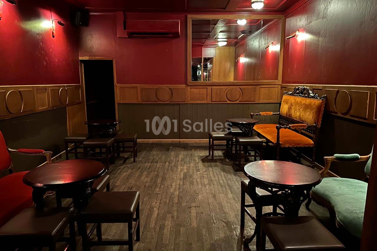 Salle intimiste avec murs rouges, mobilier en bois sombre, fauteuils colorés et éclairage tamisé.