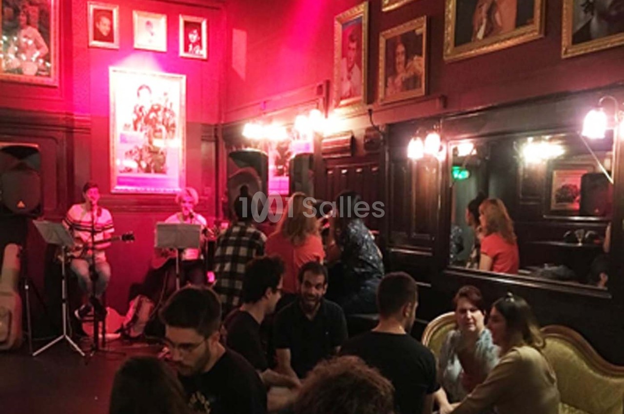 Des personnes discutent dans un café à l'ambiance chaleureuse, avec des musiciens jouant en arrière-plan.