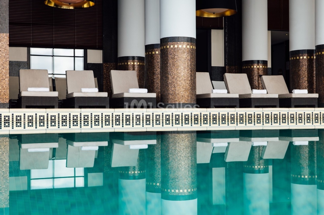 Chaises longues alignées près d'une piscine intérieure, entourée de colonnes et de décorations murales élégantes.