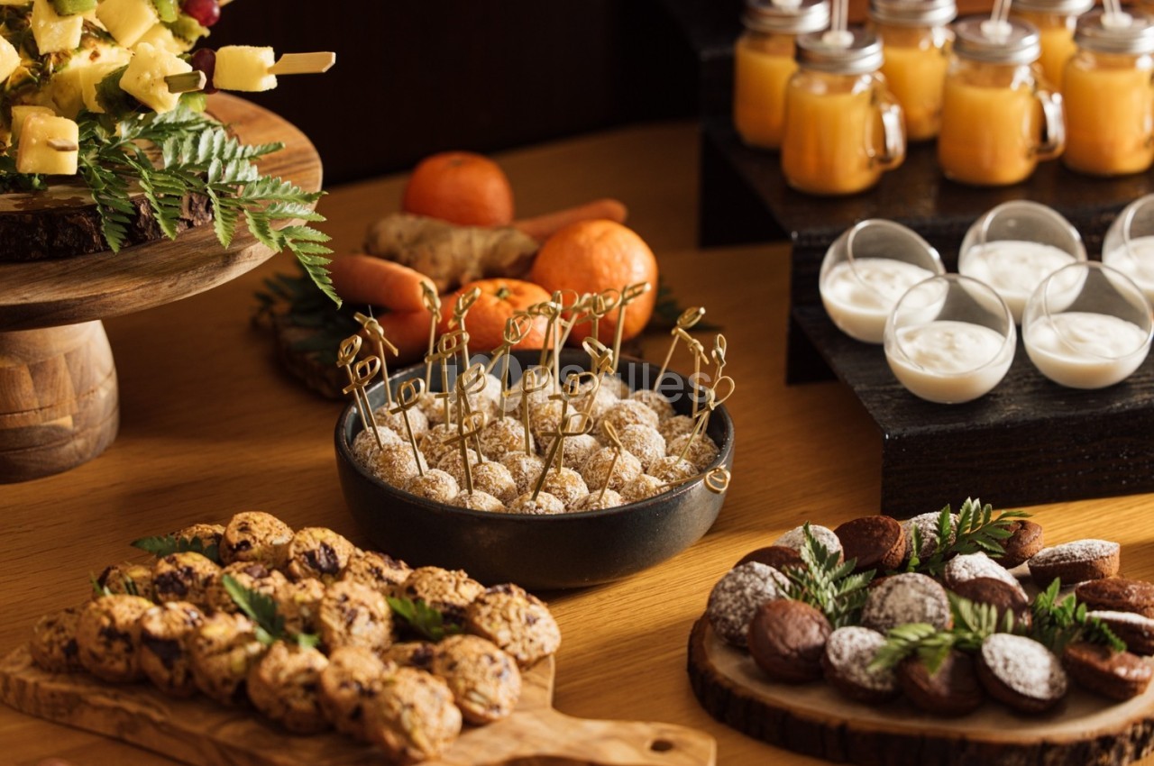 Buffet avec desserts variés, brochettes de fruits, biscuits, truffes, verrines et jus dans un cadre en bois.