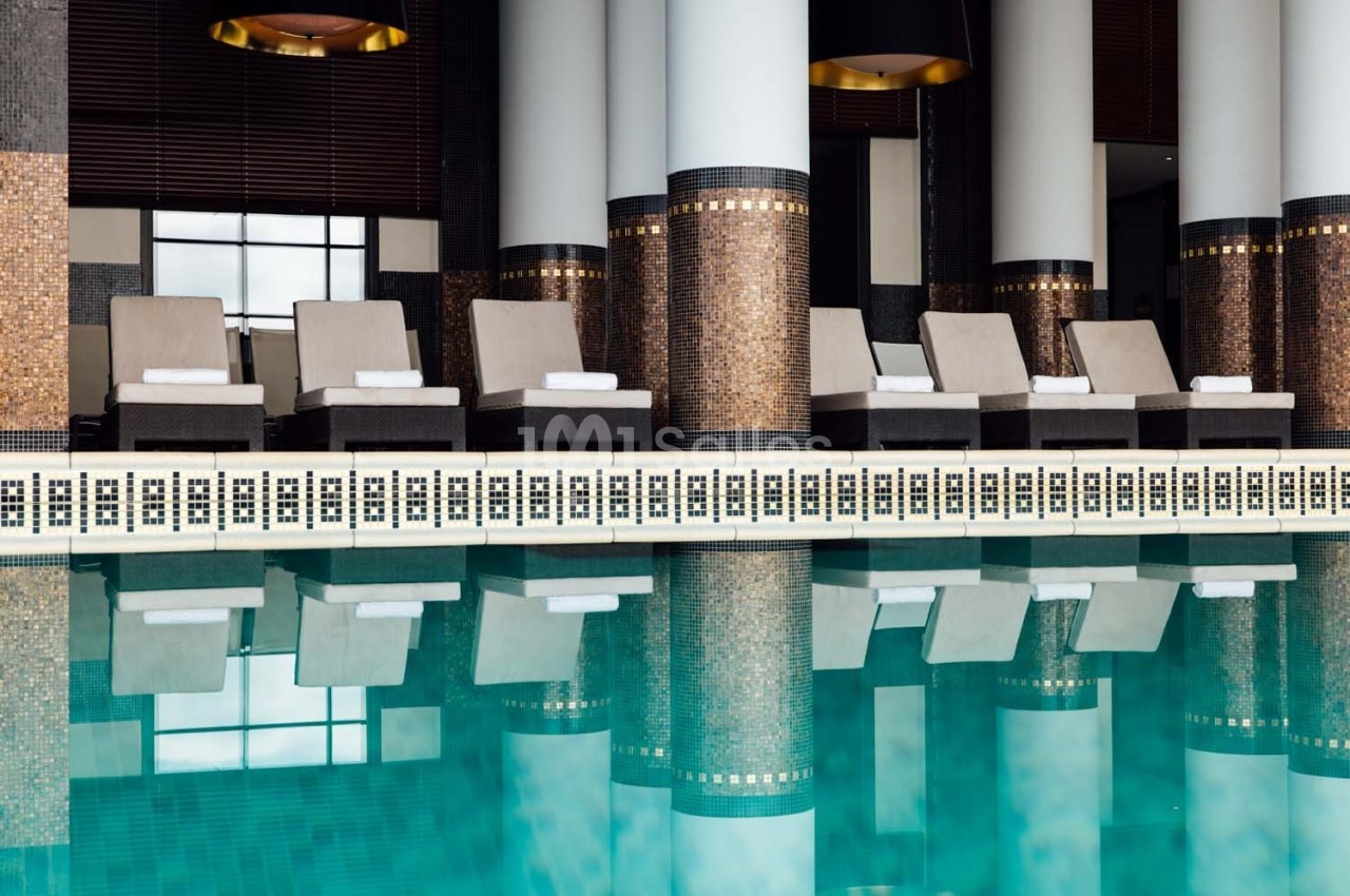 Chaises longues alignées près d'une piscine intérieure avec colonnes et mosaïques décoratives.