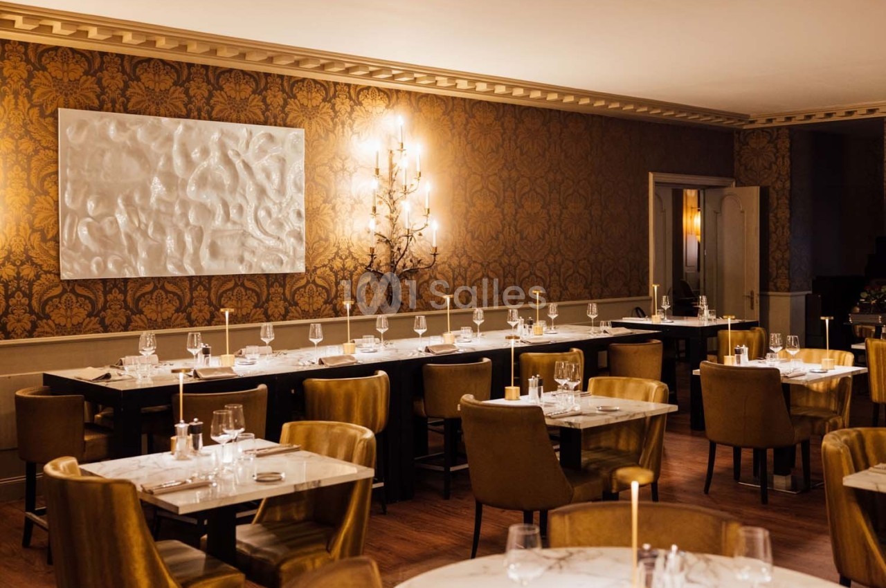 Salle de restaurant élégante avec tables dressées, chaises en velours, éclairage chaleureux et décor mural raffiné.