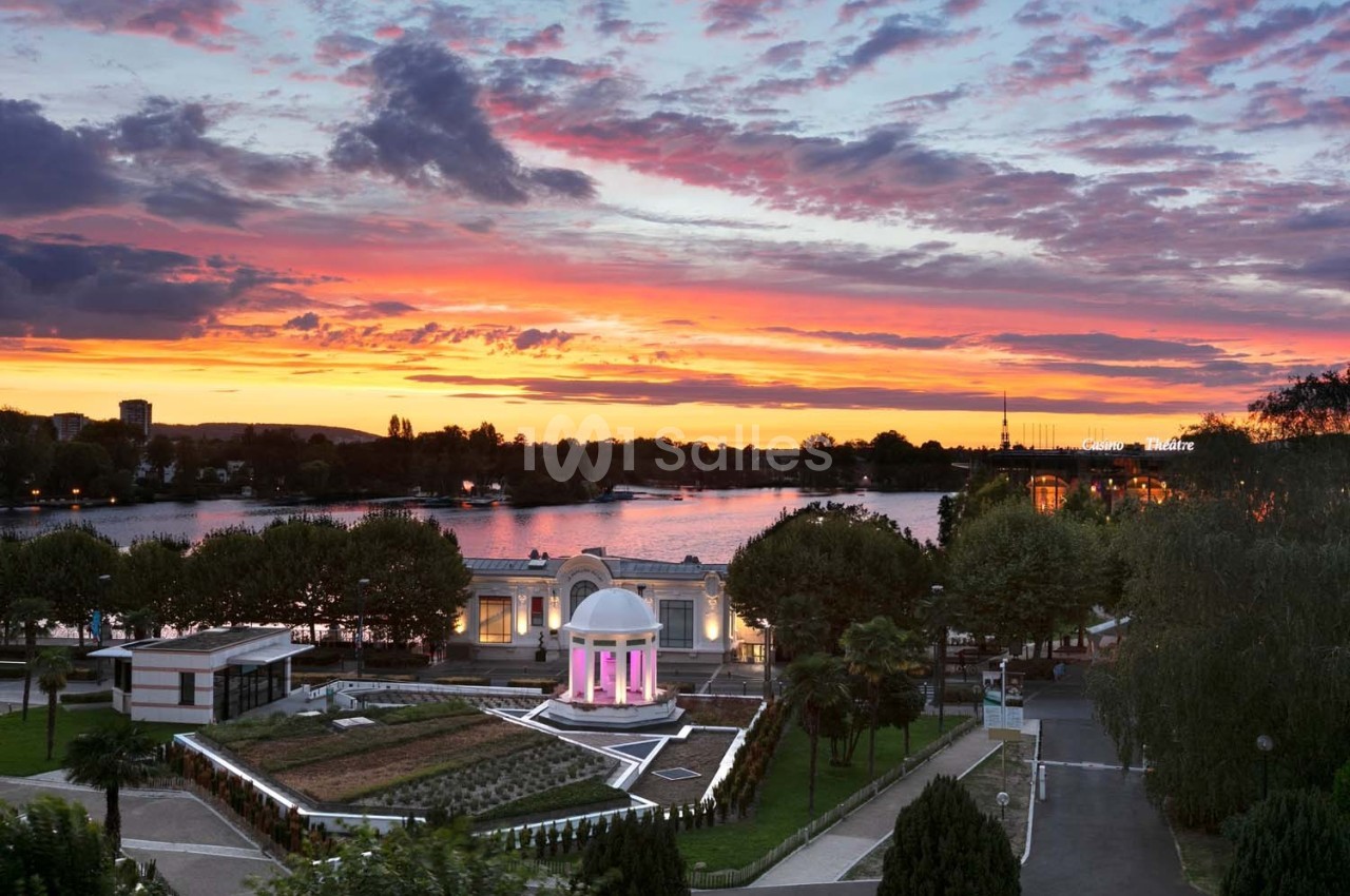 Coucher de soleil vibrant au-dessus d'un parc avec un bâtiment blanc à coupole et un lac en arrière-plan.