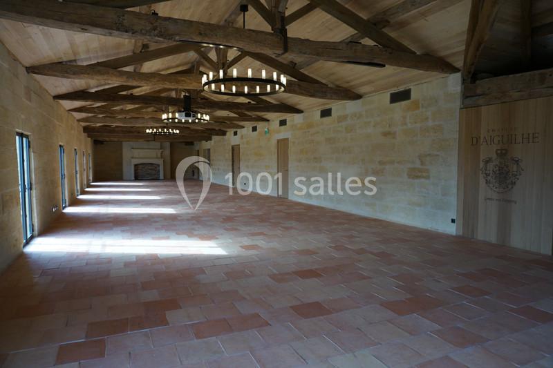 Salle spacieuse avec murs en pierre, poutres en bois apparentes et sol en carreaux de terre cuite.