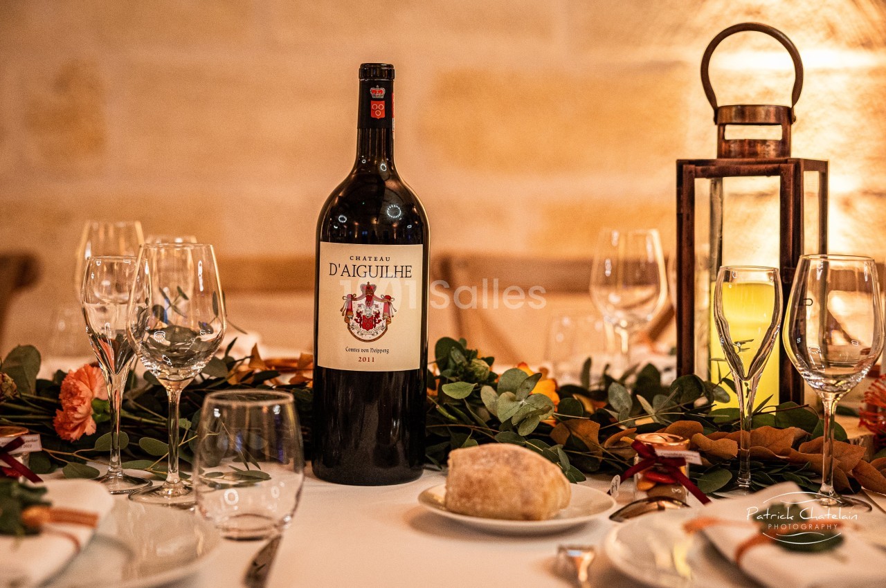Bouteille de vin rouge sur une table décorée avec des verres, des fleurs et une lanterne en arrière-plan.