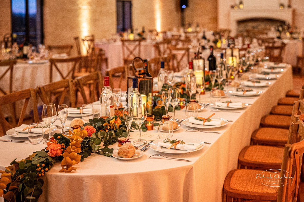 Table de réception élégamment dressée avec vaisselle, bougies, bouteilles et décoration florale dans une salle chaleureuse.